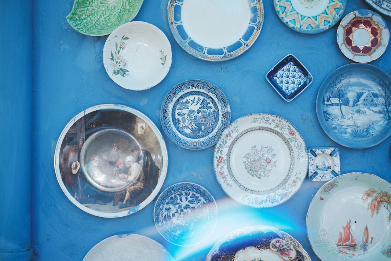about-img-01 Assorted vintage plates of different sizes and ornaments hanging on bright blue wall in light studio